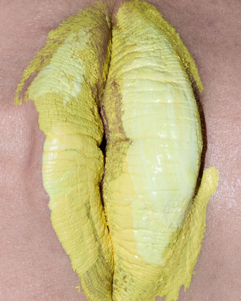 Close-up macro shot of human lips coated in textured, pale yellow cosmetic pigment.