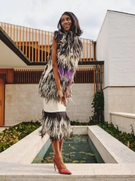 Model in feathered tunic standing beside an outdoor water feature wearing heels for 72 Magazine editorial