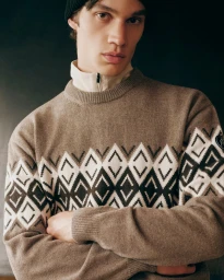 Close-up portrait of a male model wearing a brown patterned knit sweater and black beanie against a dark background.