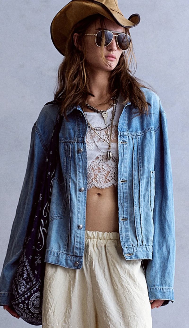 Model wearing a brown cowboy hat, aviator sunglasses, denim jacket, and cream trousers against a grey textured wall.