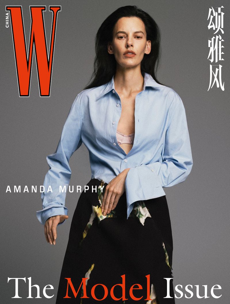 Model Amanda Murphy wearing a light blue button-down shirt and black skirt against a grey seamless backdrop