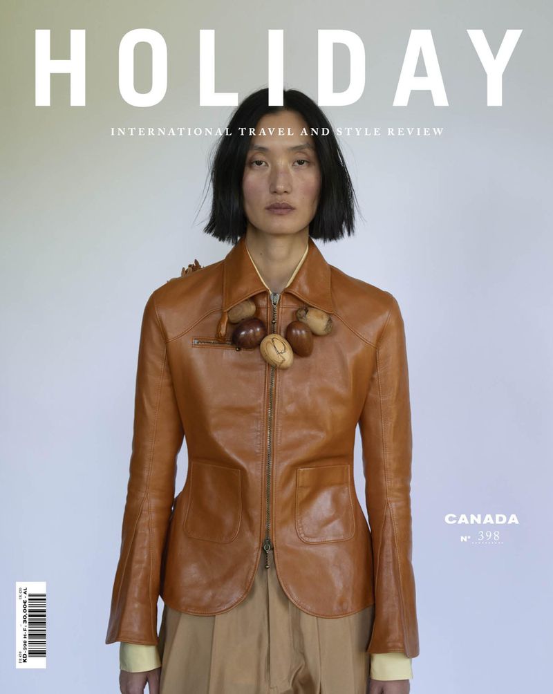 Model Lina Zhang wearing a brown leather jacket and acorn necklace against a neutral background for Holiday Magazine.