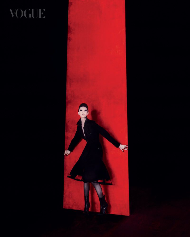 Model in a black dress standing against a vibrant vertical red panel framed by deep black background for Vogue Singapore.
