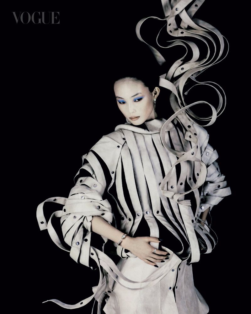 Model in sculpted strap garment with flowing ribbons against a solid black background for Vogue Singapore.