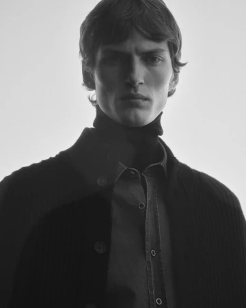 Portrait of a male model wearing a dark buttoned cardigan and turtleneck against a bright background
