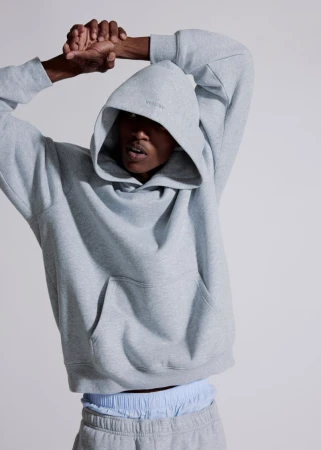 Model wearing a grey hooded sweatshirt stretching arms overhead against a seamless grey backdrop