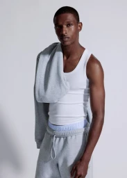 Model Malik Anderson wearing a white tank top and grey sweatpants with a hoodie draped over one shoulder against a grey background
