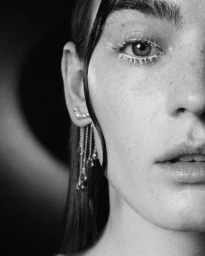 Close-up monochrome portrait of a woman with white mascara, wet hair strands, and cascading chain drop earrings for Elle Kazakhstan.