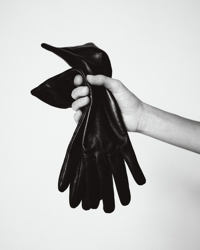 Close-up of a hand holding a pair of black leather gloves against a neutral white background for Aritzia.