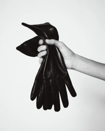 Close-up of a hand holding a pair of black leather gloves against a neutral white background for Aritzia.