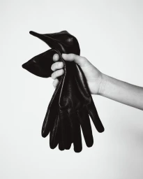Close-up of a hand holding a pair of black leather gloves against a neutral white background for Aritzia.