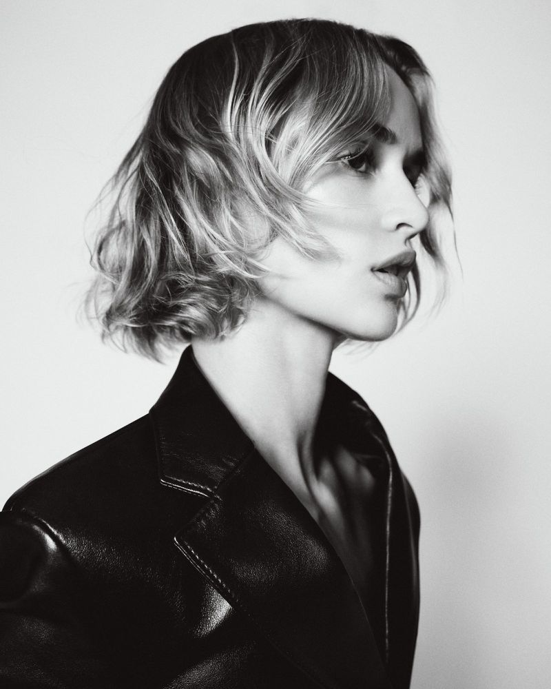 Model wearing a black leather jacket in profile against a bright white background