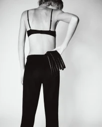 Model seen from behind wearing black trousers and holding leather gloves against a white background