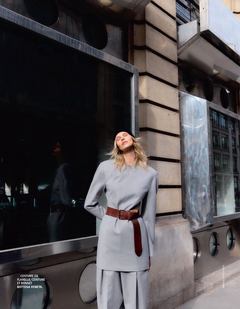 Model in grey wool suit wearing a wide brown leather belt posing outdoors against a textured stone building