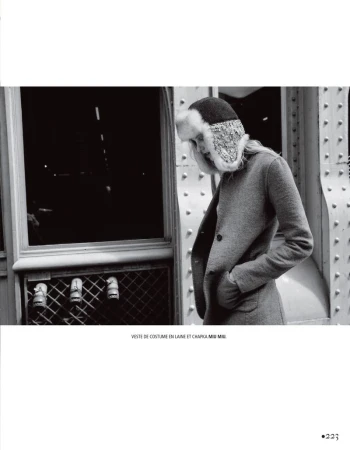 Model wearing a wool coat and fuzzy winter hat standing outdoors near an architectural iron structure
