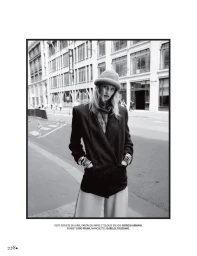 Black and white editorial photo of a female model wearing a structured blazer, trousers, and a beanie on a city street.
