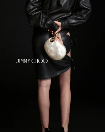 Model from behind in black leather outfit holding a pearl-like sculptural clutch for Jimmy Choo against black background.