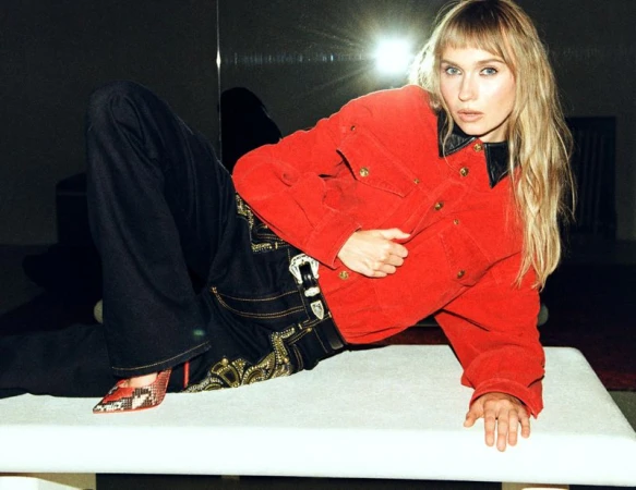 Veronika Slowikowska reclining on a white table wearing a red jacket and dark pants for Nylon Magazine