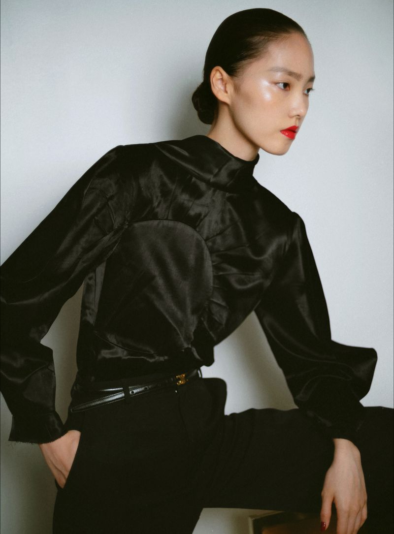 Model Jiahui Zhang wearing a black satin high-neck top and trousers against a white backdrop.
