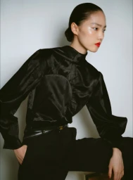 Model Jiahui Zhang wearing a black satin high-neck top and trousers against a white backdrop.