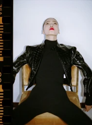 Model Jiahui Zhang seated in a gold chair wearing a black leather jacket and turtleneck for Rouge Fashionbook editorial.