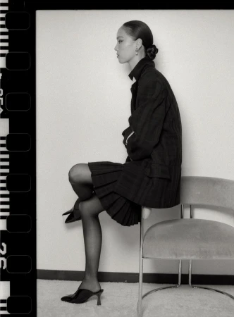 Black and white profile portrait of model Jiahui Zhang seated on an upholstered chair in a dark blazer and skirt