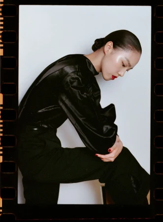 Model in black satin blouse and dark trousers with red lips against white background