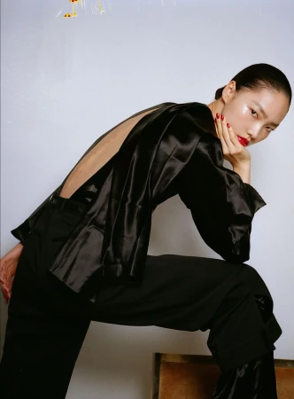 Model Jiahui Zhang wearing a black open-back satin top and dark trousers against a white backdrop for Rouge Fashionbook.