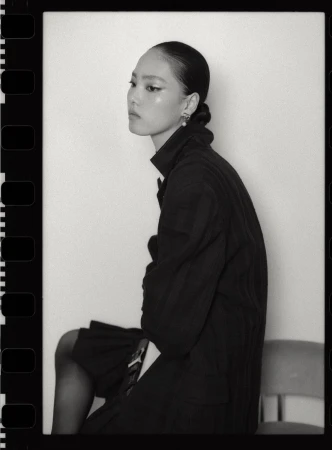 Monochrome fashion portrait of Jiahui Zhang wearing a dark jacket and skirt against a seamless white wall.