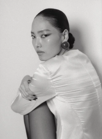 Monochrome fashion portrait of an East Asian model in a white satin top with a round dark earring looking over her shoulder.