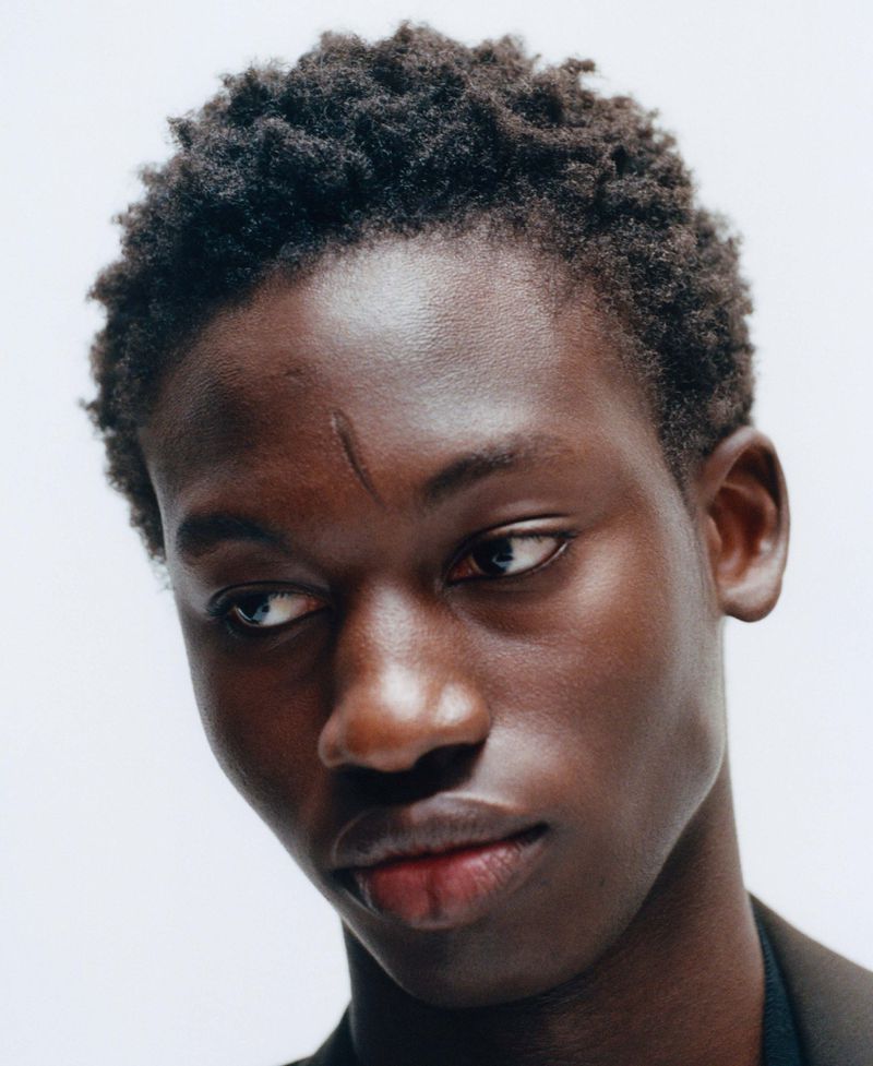 Close-up portrait of a young Black man with short textured hair and a light scar on his forehead against a white seamless background