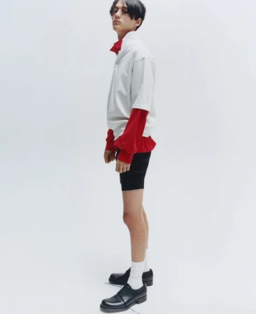 Young male model posing in profile wearing a layered white and red shirt against a plain white background.