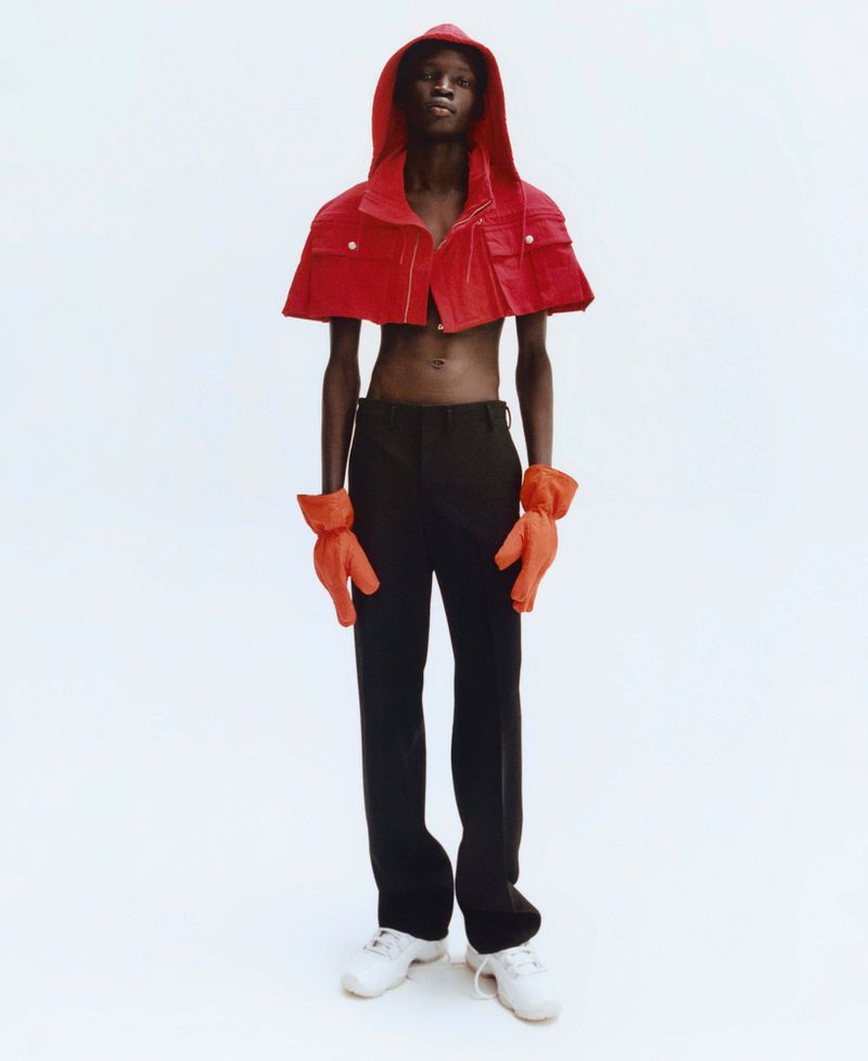 Model wearing a cropped red hooded jacket and orange gloves against a white background