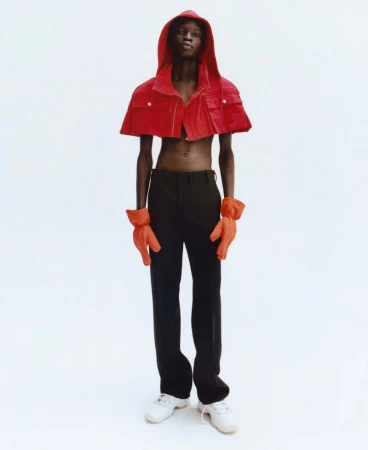 Model wearing a cropped red hooded jacket and orange gloves against a white background