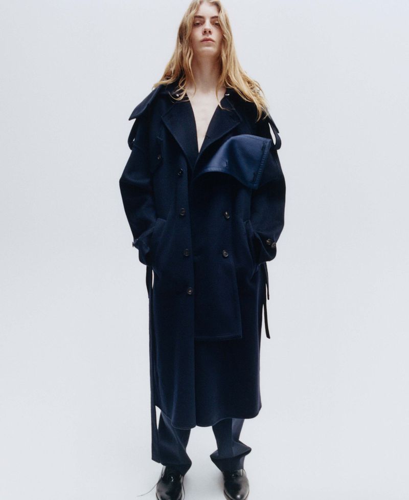 Model with long blonde hair wearing a dark navy wool coat against a plain white studio background.