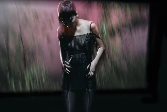 Model in dark strapless dress standing against a blurry abstract pink and green projection backdrop