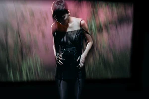 Model in dark strapless dress standing against a blurry abstract pink and green projection backdrop