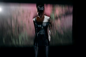 Model in a black dress standing against a projected pink and green motion-blurred backdrop