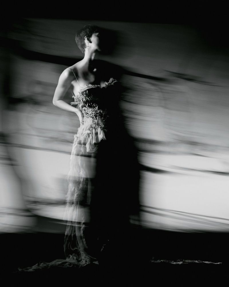 Model in a textured dress captured with motion blur in a high-contrast black and white editorial fashion photograph.