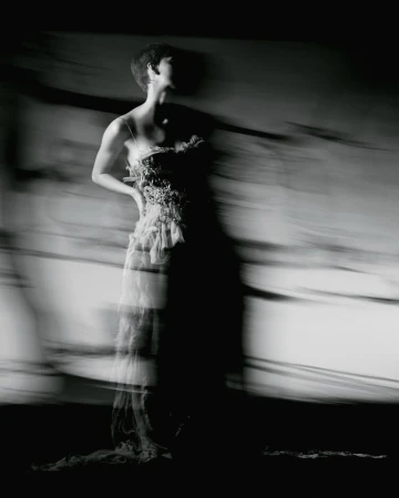 Model in a textured dress captured with motion blur in a high-contrast black and white editorial fashion photograph.