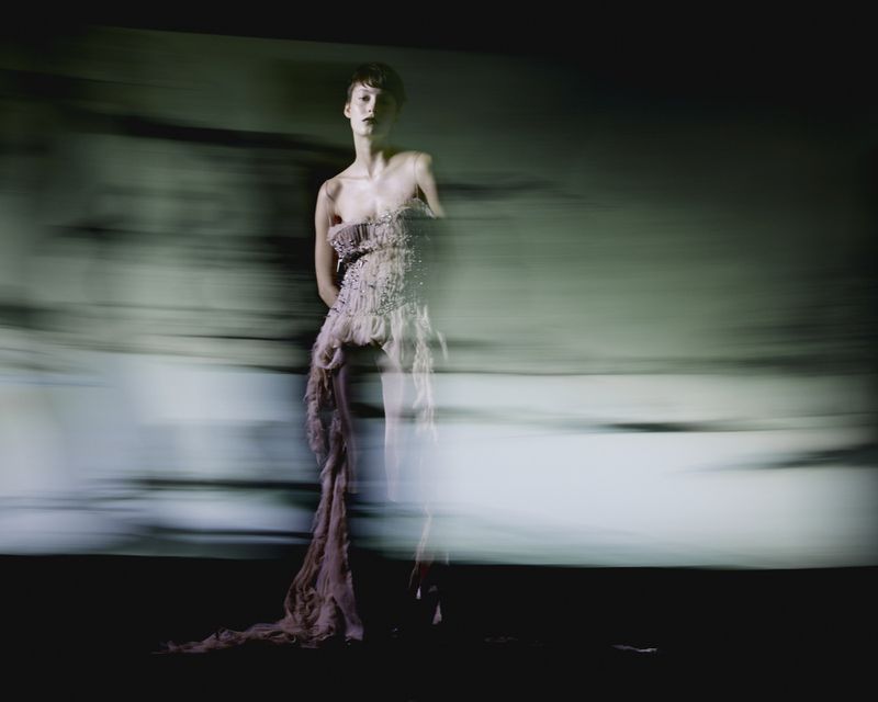 Model in a textured strapless gown captured with horizontal motion blur against a dark abstract background for Vogue Portugal.