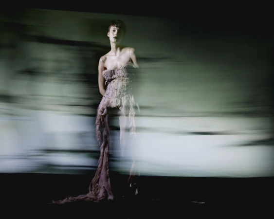 Model in a textured strapless gown captured with horizontal motion blur against a dark abstract background for Vogue Portugal.