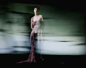Model in a textured strapless gown captured with horizontal motion blur against a dark abstract background for Vogue Portugal.