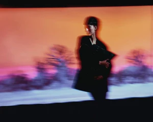 Model with motion blur standing in front of a colourful projected sunset landscape for Vogue Portugal