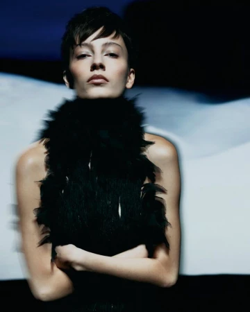 Model with short dark hair wearing a black feathered top against a dark and blurred background for Vogue Portugal.