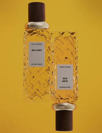 Two glass perfume bottles with textured patterns and wooden caps set against a vibrant yellow background