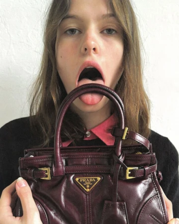 Model holding a glossy burgundy Prada handbag up to her mouth with tongue out for Numéro New York
