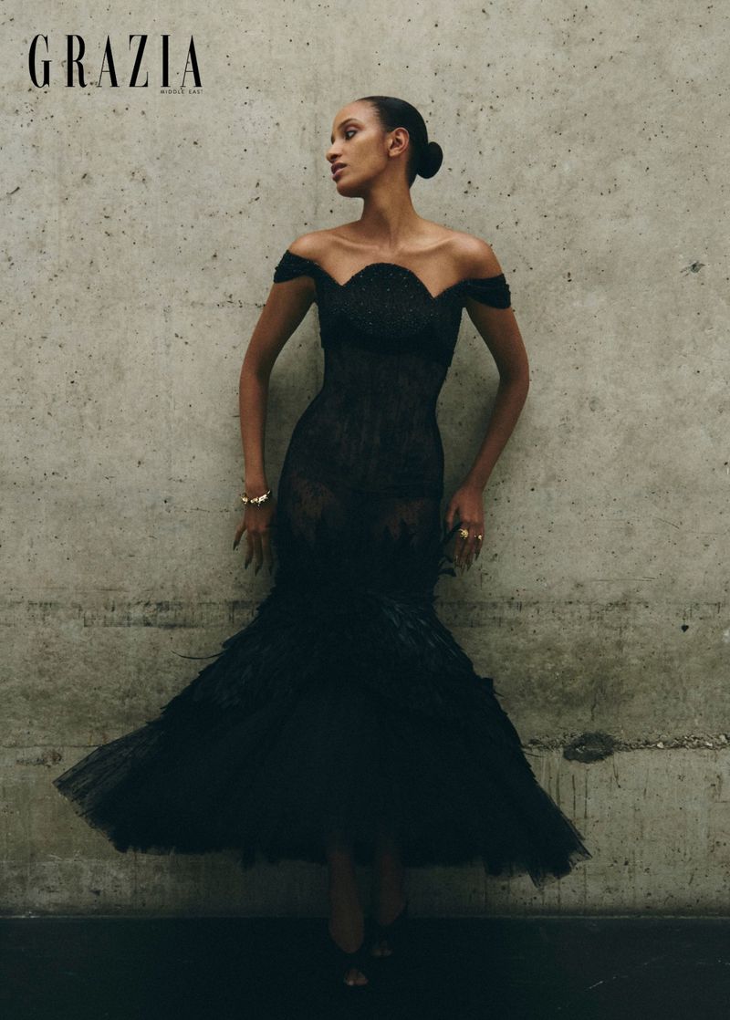 Model in off-the-shoulder black gown against textured concrete wall for Grazia Middle East