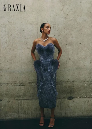 Model in a strapless textured grey feather dress standing against a mottled concrete wall