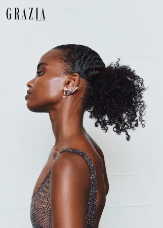 Profile portrait of a Black female model wearing an ornate jewelled ear cuff and a sparkling dress against a white background